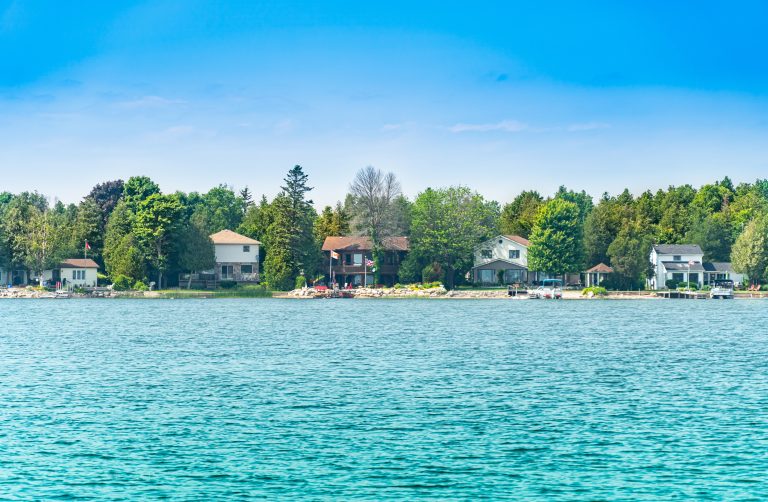 Cottages by Lake Huron shoreline in Pike Bay, surrounded by forest at summer day. Cottages for seasonal vacation rent and personal leisure